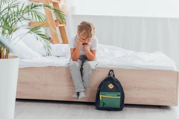 Upprörd Pojke Pyjamas Sitter Sängen Nära Skolan Ryggsäck Golvet — Stockfoto