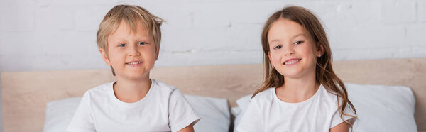 horizontal image of brother and sister in white t-shirts looking at camera in bedroom