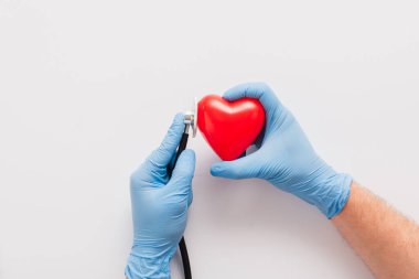 cropped view of doctor in latex gloves examining red heart with stethoscope on white background clipart
