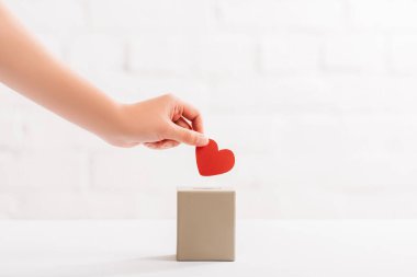cropped view of female hand putting red heart in box on white background, donation concept clipart
