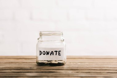 penny jar with donate lettering on wooden surface on white background clipart