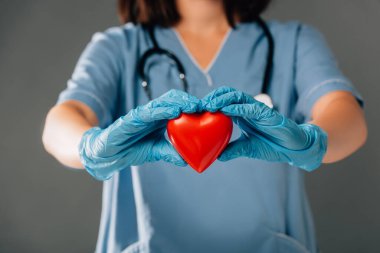 cropped view of doctor with stereoscope in latex gloves holding red heart isolated on grey clipart