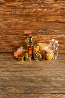 groats near water, oil, canned food and honey on wooden background, charity concept clipart