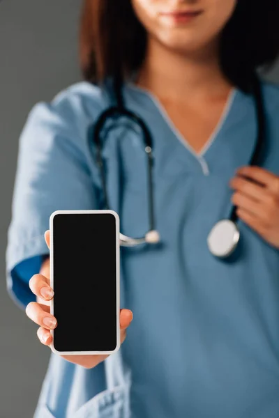 スマートフォンを持ったステレオスコープを持った医師とグレーで隔絶された空白の画面 — ストック写真