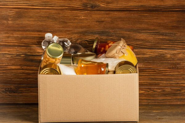 картонная коробка с пожертвованной пищей на деревянном фоне, концепция благотворительности