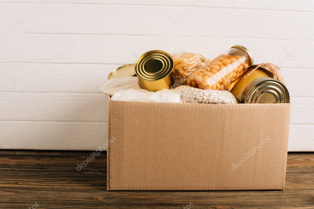 cardboard box with donated food on wooden background, charity concept
