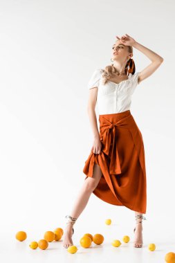 Beyaz arka planda narenciye meyvelerinin yanında poz veren zarif sarışın kadın.