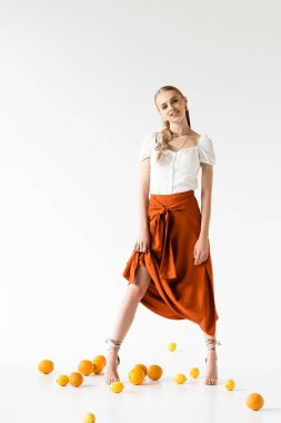 Beyaz arka planda narenciye meyvelerinin yanında poz veren zarif sarışın kadın.