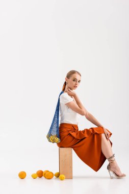 Beyaz arka planda dağınık narenciye meyvelerinin yanında iple poz veren zarif sarışın kadının yan görüntüsü