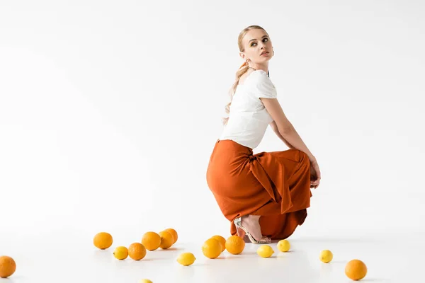 白地に柑橘系の果実の近くにポーズをとるエレガントなブロンドの女性の側面図 — ストック写真