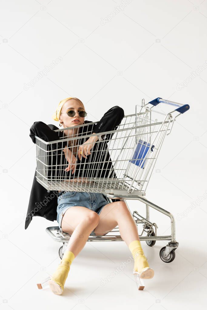 fashionable woman in black and yellow outfit posing with shopping cart on white