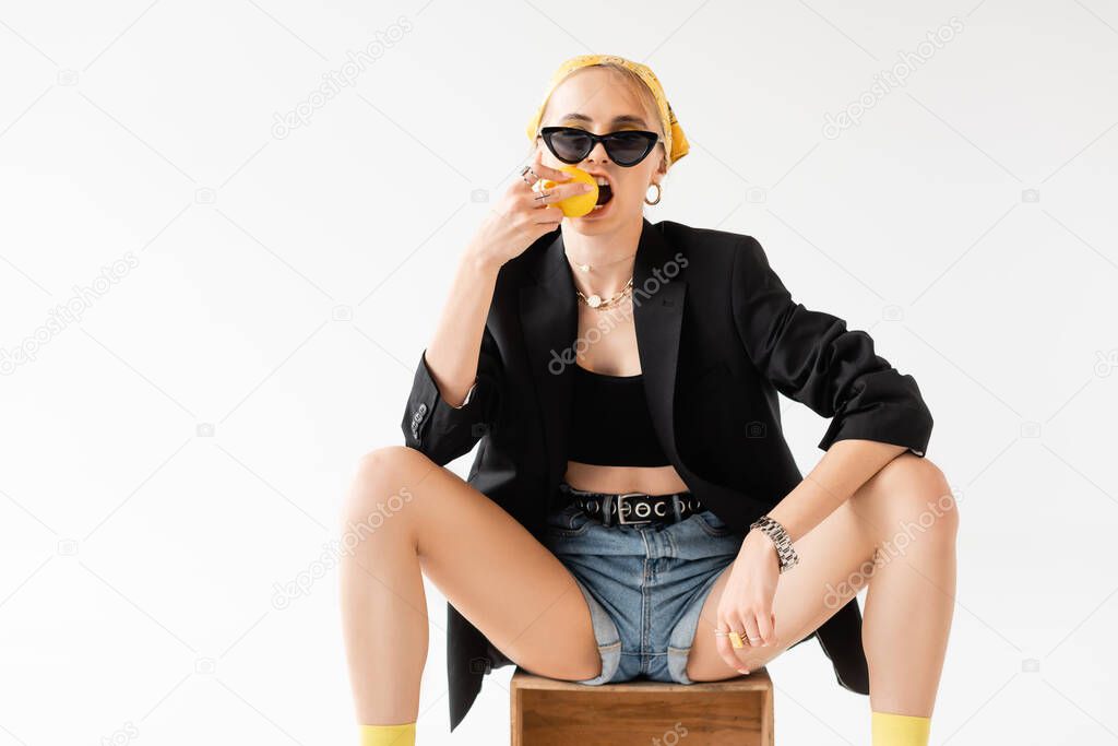 fashionable woman biting lemon on wooden box isolated on white