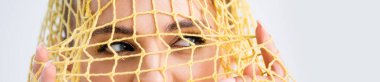 cropped view of woman looking through yellow string bag on white background, panoramic shot clipart