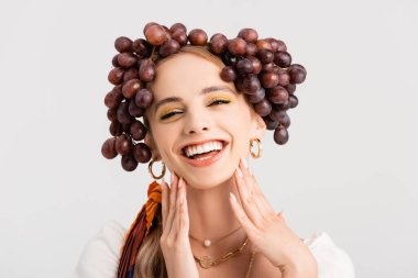 Kafasında üzümlerle poz veren kırsal sarışın kadın beyaz üzerinde izole edilmiş.