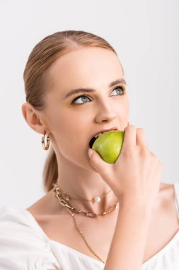 Sarışın kadın yeşil elmayı ısırıyor ve tek başına beyaz elmaya bakıyor.