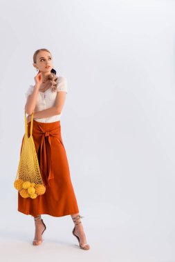 rüya gibi bir sarışın kadın turunçgillerle poz veriyor sarı iplik torbasında beyaz üzerinde izole edilmiş.