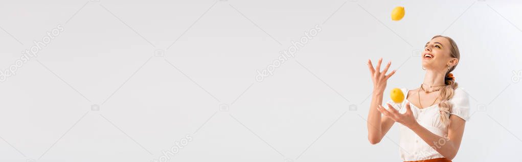 blonde woman juggling with yellow lemons isolated on white, panoramic shot