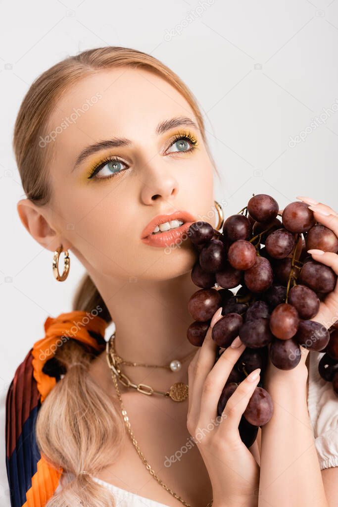 rustic blonde woman posing with grapes and looking away isolated on white