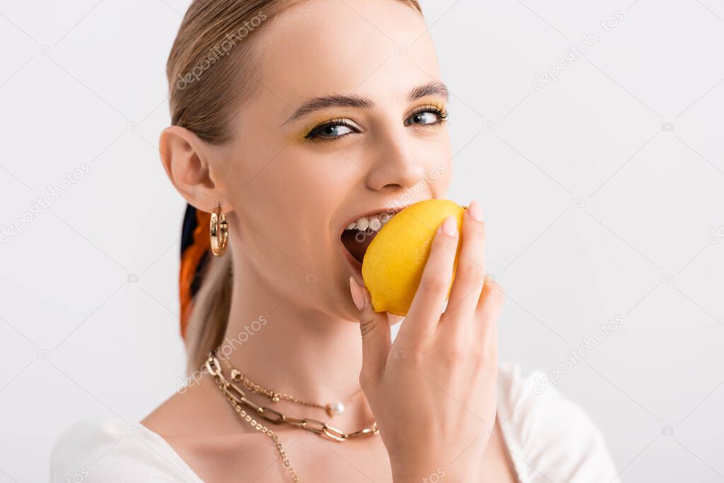 rustic blonde woman biting yellow lemon isolated on white