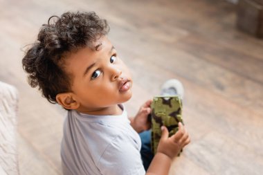 overhead view of curly african american child looking at camera while holding toy clipart
