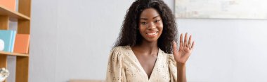 Afro-Amerikan kadının kameraya bakarken el sallamasının yatay görüntüsü.