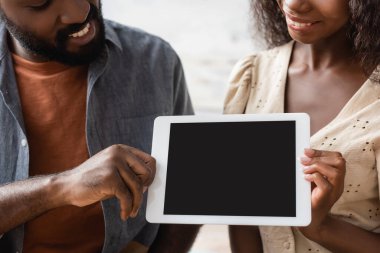 Afro-Amerikan bir adamın elinde dijital tabletle evde karısının yanında boş ekranlı görüntüsü.