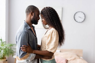 Afro-Amerikan karı-kocanın gündelik kıyafetleri içinde yatak odasında yüz yüze dururken yan görünüşü.