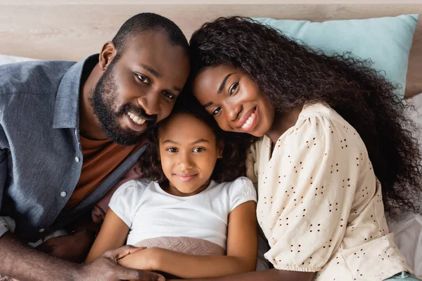 非洲裔美国人夫妇躺在床上看着女儿近旁的相机的高视角照片 — 图库照片