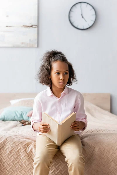 Nachdenkliches Afrikanisch Amerikanisches Mädchen Sitzt Mit Buch Bett Und Schaut — Stockfoto