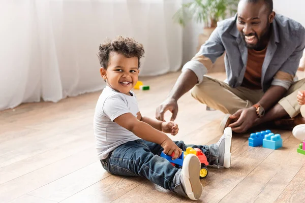 Emocionado Afroamericano Hombre Cerca Hijo Jugando Con Juguete Camión Piso — Foto de Stock