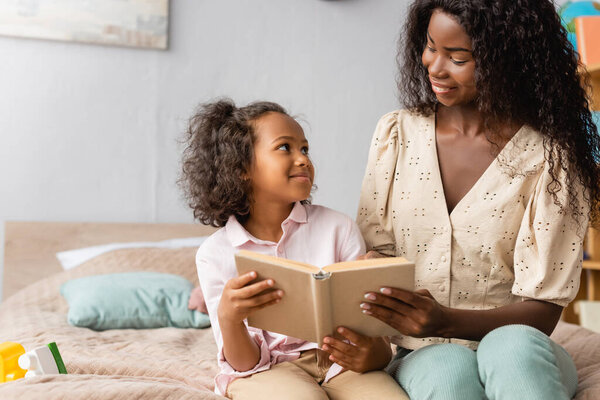 african american mom and child looking at each other while reading book together