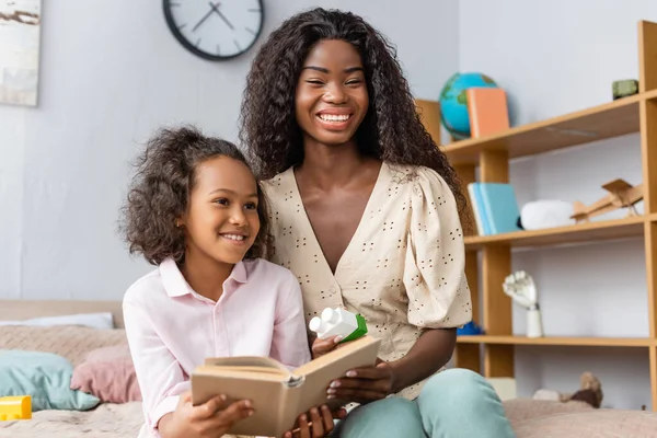 Afrikanska Amerikanska Flicka Hålla Bok Medan Sitter Sovrum Med Mamma — Stockfoto