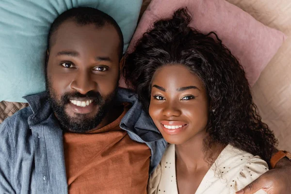 top view of young african american american husband and wife lying in bed in casual clothes