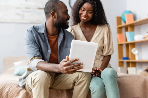 アフリカ系アメリカ人男性がベッドに座りながら妻にデジタルタブレットを見せ — ストック写真