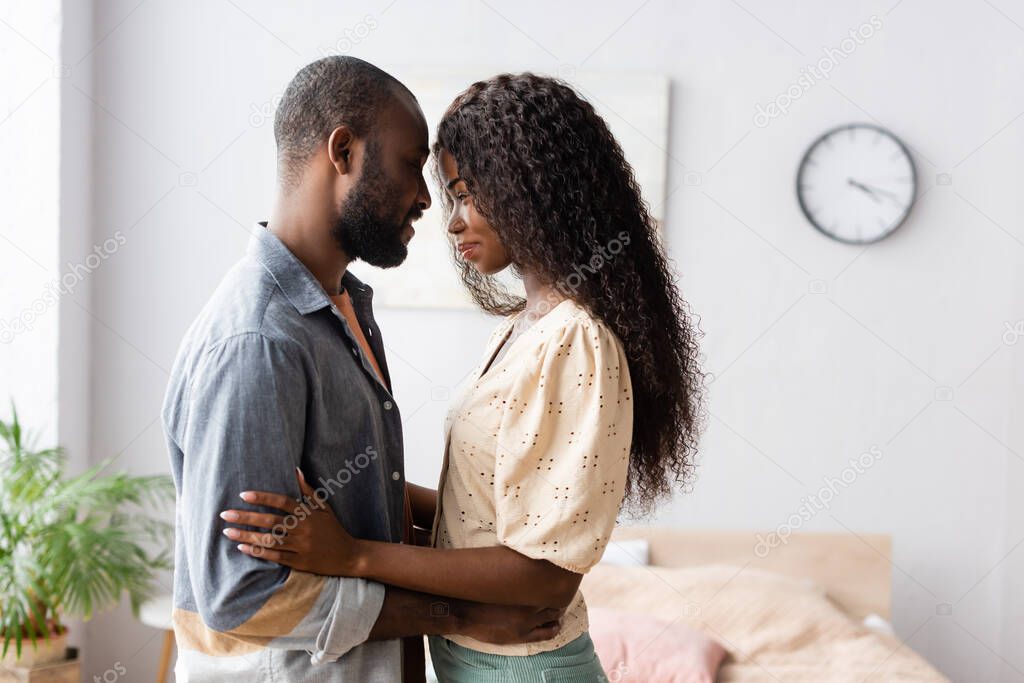 side view of african american husband and wife in casual clothes standing face to face in bedroom