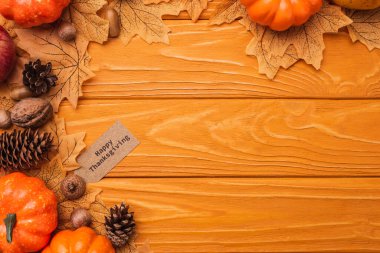top view of pumpkins, autumnal decoration and happy thanksgiving card on wooden background clipart