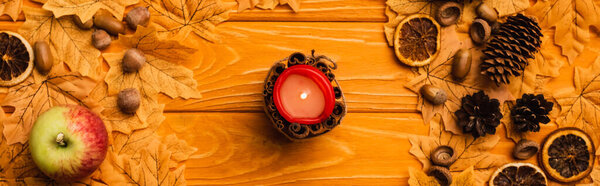 top view of burning candle with autumnal decoration on wooden background