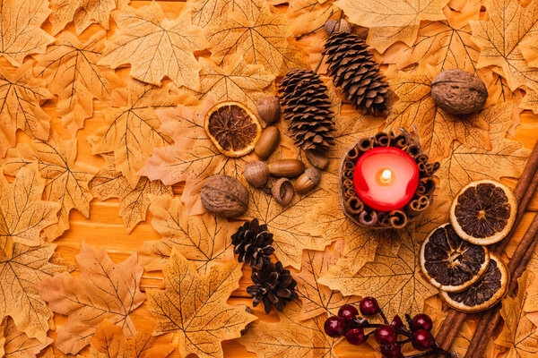 top view of burning candle with autumnal brown decoration on golden foliage