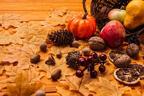 Осенние украшения и продукты питания, разбросанные из плетеной корзины на золотой листве на деревянном фоне