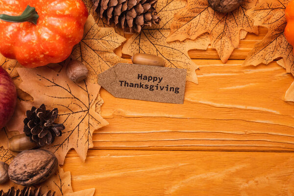 top view of pumpkin, autumnal decoration and happy thanksgiving card on wooden background