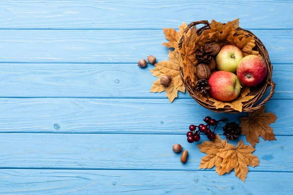 青い木の背景にりんごやナッツやコーンが入った秋のウィッカーバスケットの上からの眺め — ストック写真