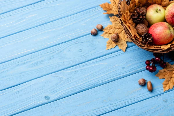 青い木の背景にりんごやナッツやコーンが入った秋のウィッカーバスケットの上からの眺め — ストック写真