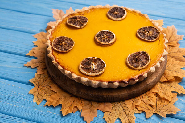 decorated pumpkin pie with golden foliage on blue wooden background