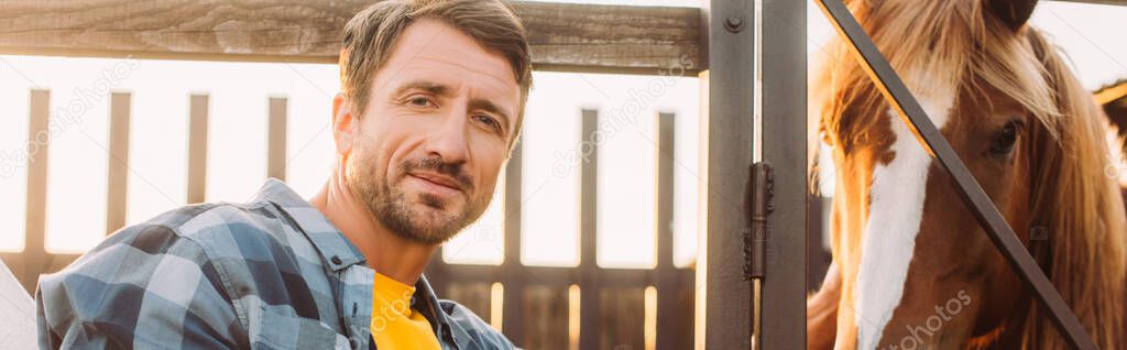 horizontal concept of farmer in plaid shirt looking at camera near horse in corral on farm