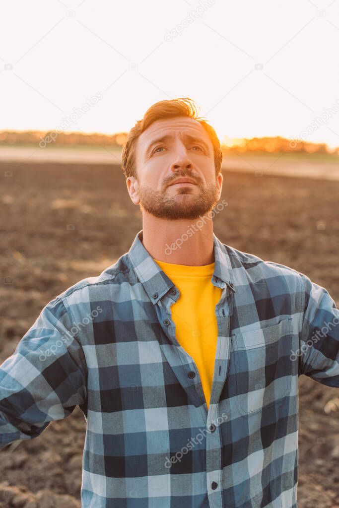 rancher in checkered shirt looking up while standing on plowed field