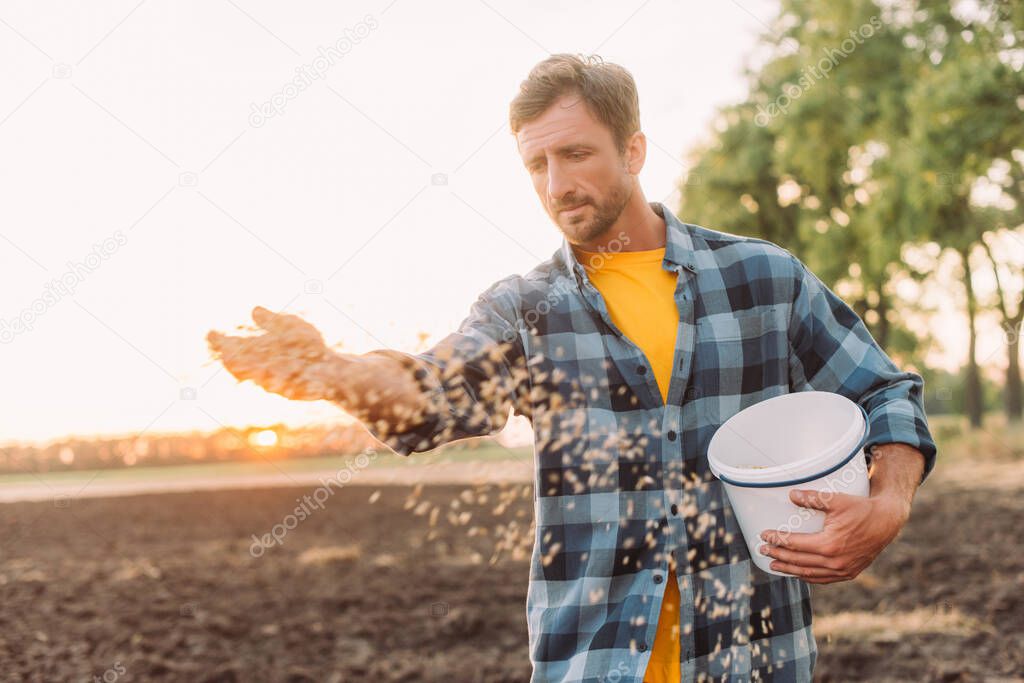 selective focus of farmer in plaid shirt sowing seeds on plowed field