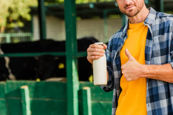 农民拿着一瓶鲜牛奶 在牛棚附近竖起大拇指的局部图像 — 图库照片