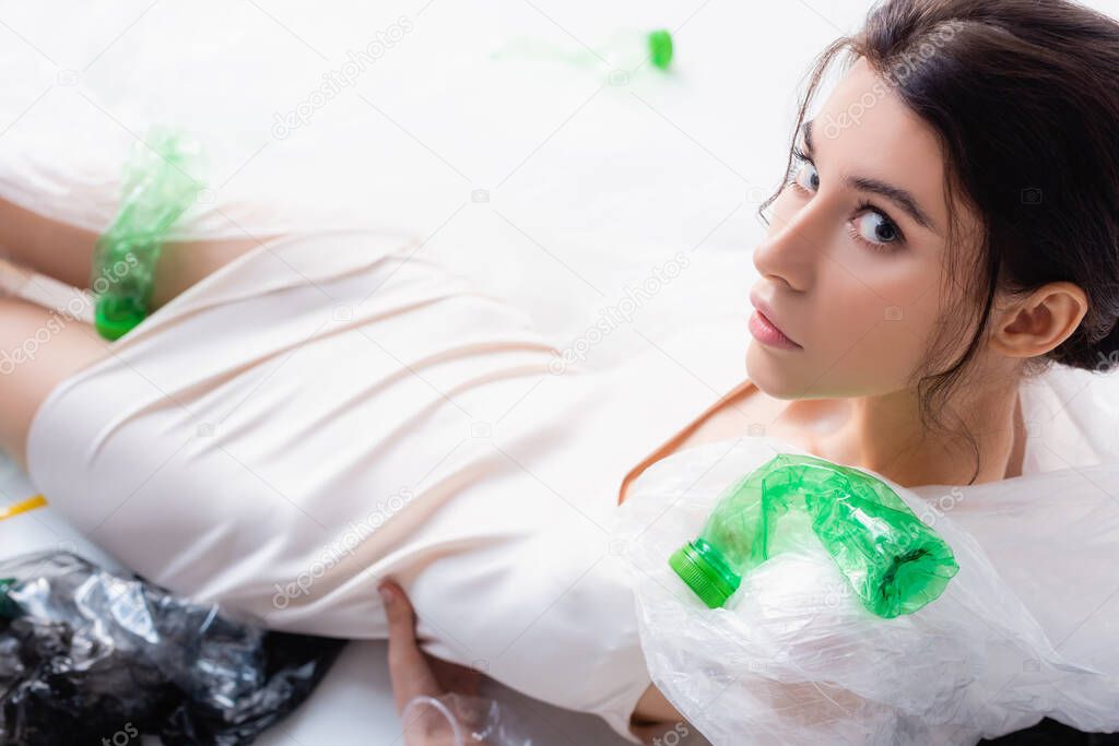 high angle view of woman sitting near empty bottles, plastic bags and spoons on white, ecology concept  