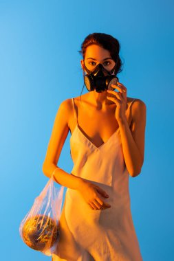 Kadın gaz maskesine dokunuyor ve elinde mavi kürenin olduğu plastik bir çanta tutuyor, ekoloji kavramı. 