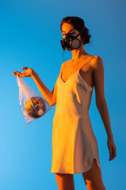 Gaz maskeli genç bir kadın elinde mavi küreli plastik bir çanta, ekoloji kavramı. 